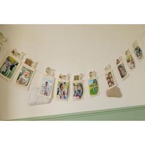 May include: A photo banner with pictures of children and families. The banner is strung across a white wall and includes wooden cutouts of a train, hot air balloon, and suitcases. The photos are held by small wooden clips.