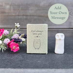 Könnte beinhalten: Eine kleine weiße Keramik-Eulenfigur mit einer braunen Schachtel, auf der "Owl always love you" mit einem kleinen Herzen steht.
