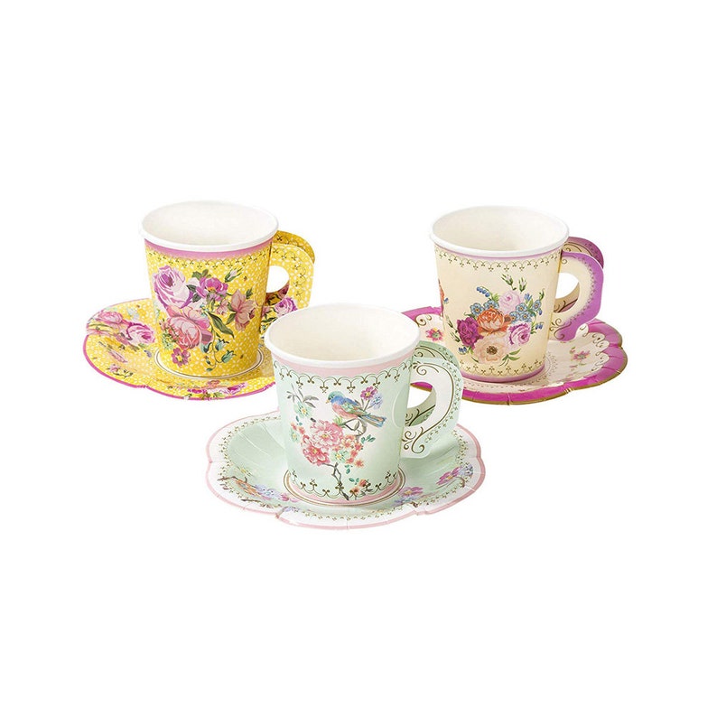 May include: Three paper teacups and saucers with floral patterns. The cups have a yellow, green, and cream background with pink, red, and blue floral designs. The saucers have scalloped edges and matching floral patterns.
