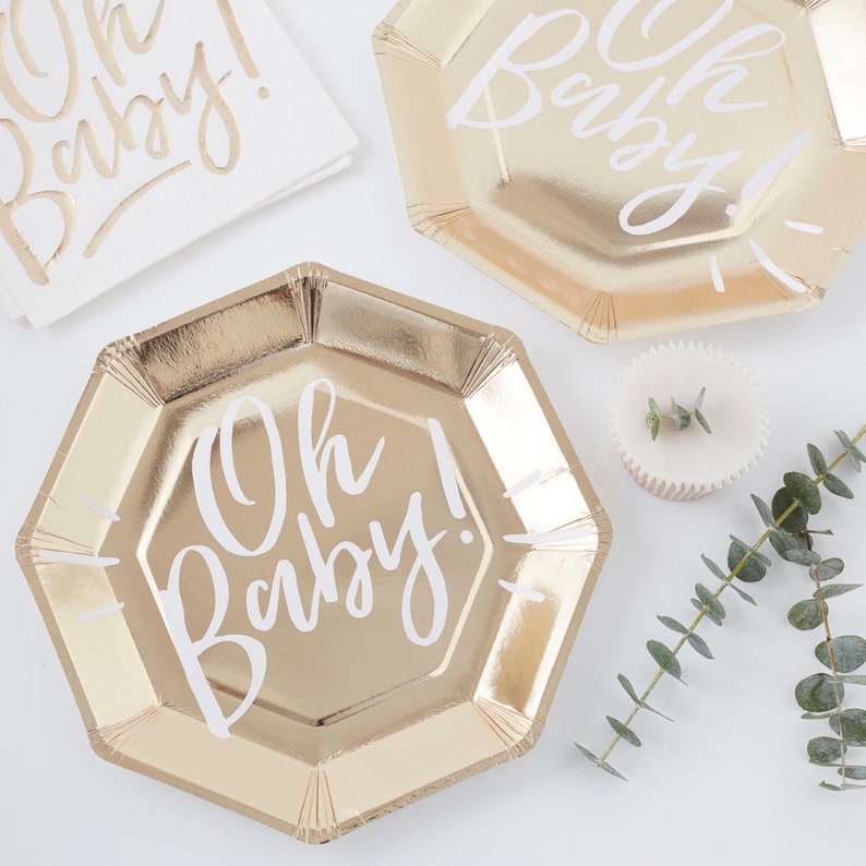 May include: Gold paper plates with a white "Oh Baby!" inscription. The plates are octagonal and have a metallic sheen.