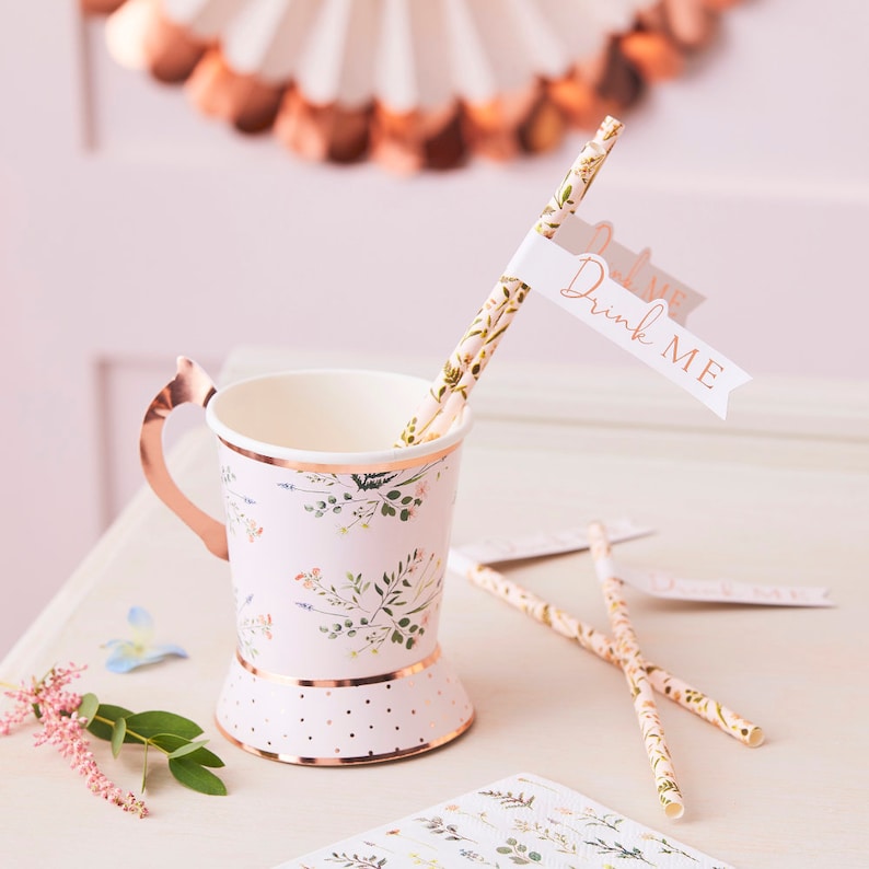 K&ouml;nnte beinhalten: Ein Set aus rosa und gr&uuml;nen floralen Papierstrohhalmen mit einer wei&szlig;en Flagge, auf der in goldenen Buchstaben "Drink Me" steht. Die Strohhalme befinden sich in einem rosa und gr&uuml;nen floralen Papierbecher mit goldfarbenem Rand und Henkel.