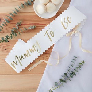 May include: White sash with gold lettering that says "Mommy To Be" with a gold ribbon attached.