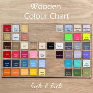Pu&ograve; includere: Una tabella colori in legno con una griglia di piccoli campioni quadrati in varie tonalit&agrave;, inclusi colori glitterati, iridescenti, fluorescenti e pieni. Il testo "Wooden Colour Chart" appare in alto e "luck & luck" in basso.