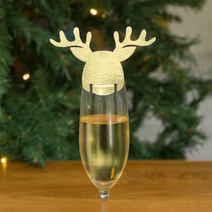 May include: Gold reindeer shaped glass marker for a champagne flute. The reindeer is made of paper and has a gold finish.