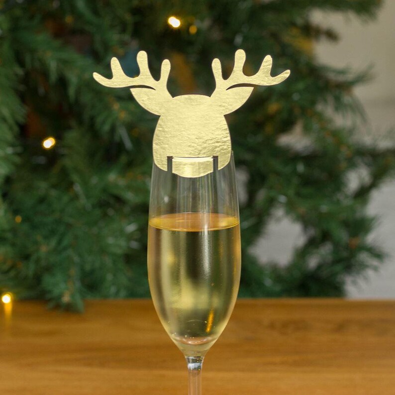 May include: Gold reindeer shaped glass marker for a champagne flute. The reindeer is made of paper and has a gold finish.