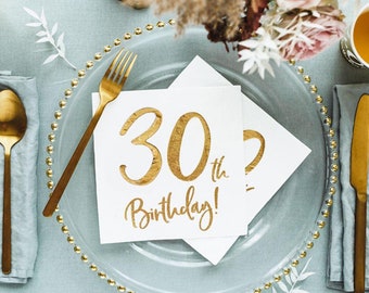 May include: A festive table setting with a clear glass plate, gold cutlery, and white napkins. The napkins are printed with "30th Birthday!" in gold script. The scene includes flowers and a light blue tablecloth, creating an elegant birthday celebration theme.