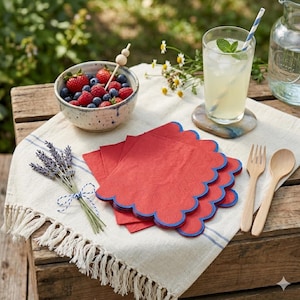 Puede incluir: Una escena de picnic con un cuenco de bayas, servilletas rojas con bordes festoneados azules, un vaso de limonada con pajita y cubiertos de madera. También hay un ramo de lavanda y una brocheta decorativa. El escenario es al aire libre.