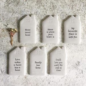 May include: Six white ceramic house-shaped ornaments with different quotes about home and family. The quotes are: "Love makes a house into a home", "Home sweet home", "Home is where your heart is", "Family love home", "My favorite place is with you", and "I will love you until the end of time".