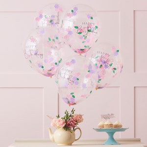 K&ouml;nnte beinhalten: F&uuml;nf transparente Ballons mit rosa und violettem Konfetti und dem aufgedruckten Text "Happy Birthday". Die Ballons sind zusammengebunden und schweben vor einer rosa Wand.