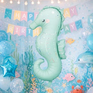 Puede incluir: Un gran globo con forma de caballito de mar verde menta con detalles plateados. El globo forma parte de una escena de cumpleaños con globos azules y una pancarta que dice "Happy Birthday". El globo mide unos 100 cm de altura.