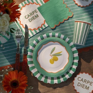 Puede incluir: Una mesa decorada con platos, vasos y servilletas de papel a rayas verdes y blancas. Los platos tienen un borde festoneado y un diseño de rama de olivo. Una servilleta y un posavasos dicen "CARPE DIEM". También hay un tenedor y un cuchillo.