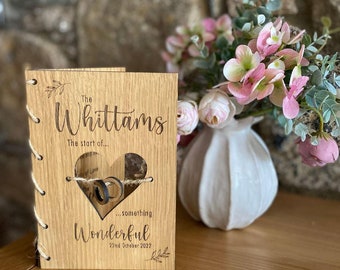 May include: A wooden guest book with a heart-shaped cutout for rings. The book is engraved with "The Whittams The start of... something Wonderful 22nd October 2022".