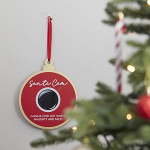 Może przedstawiać: Czerwona i złota ozdoba choinkowa w kształcie aparatu fotograficznego z tekstem "Santa Cam" i "Gonna find out who's naughty and nice!"