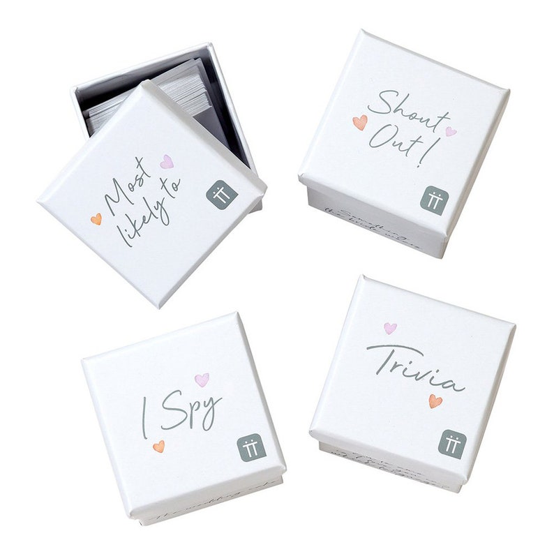 May include: Four white boxes with different game titles printed on them. The boxes are labeled "Most Likely To", "Shout Out!", "I Spy", and "Trivia". Each box has a small pink heart and a small orange heart printed on it.