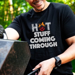 May include: A black t-shirt with a white graphic that says "HOT STUFF COMING THROUGH" with a red and orange flame and a grill utensil icon.