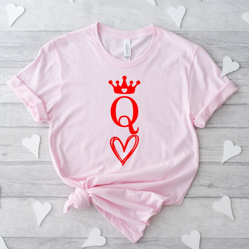 May include: Pink t-shirt with a red graphic of a queen of hearts playing card with a crown and a heart.