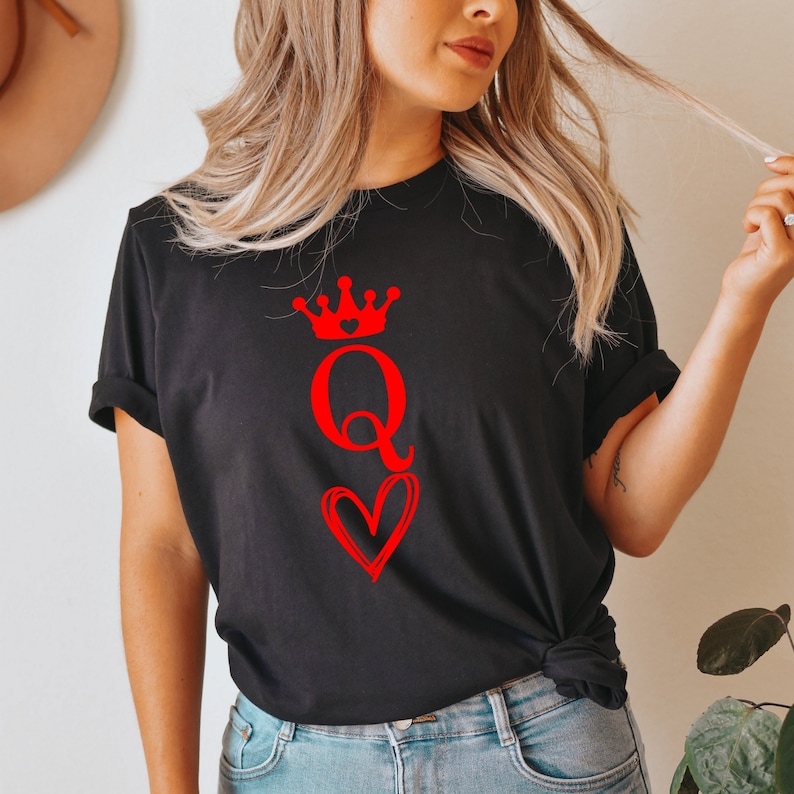 May include: Black t-shirt with a red graphic of a queen of hearts playing card. The queen is wearing a crown and holding a heart.
