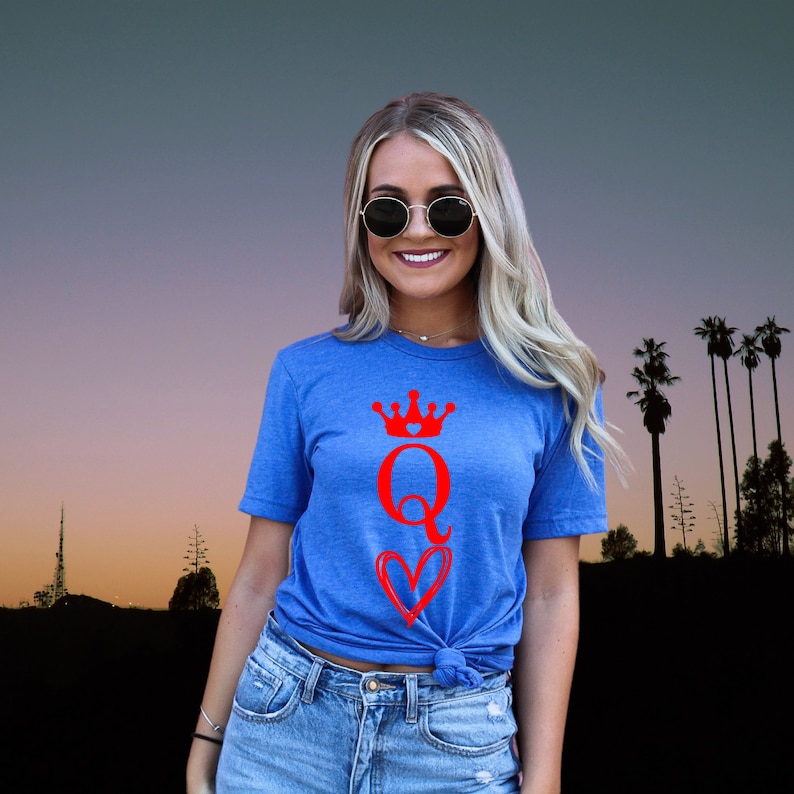 May include: A royal blue t-shirt with a red graphic of a queen of hearts playing card. The graphic features a crown, the letter Q, and a heart.