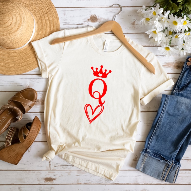 May include: A white t-shirt with a red queen of hearts design. The queen is wearing a crown and holding a heart.