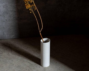 May include: A white ceramic vase with a rough texture holds a dried flower stem with yellow blooms.
