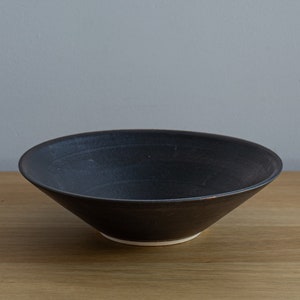 May include: A wide, black ceramic bowl with a white rim. The bowl is sitting on a wooden surface.