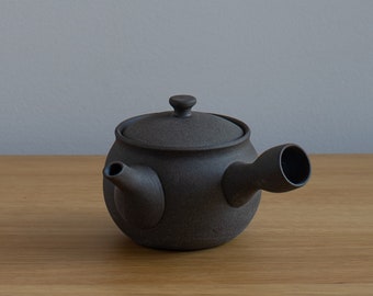 May include: A dark brown ceramic teapot with a rounded body, a lid with a small knob, and a curved spout. The teapot has a textured surface and is designed for brewing tea.