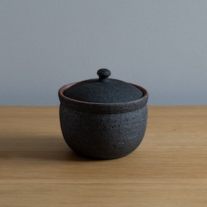 May include: A black ceramic jar with a lid, the jar has a rough texture and the lid has a small knob on top.