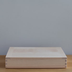 May include: A light wood box with a hinged lid. The box is closed and sitting on a wooden surface.