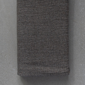 May include: A dark gray woven fabric napkin, folded in half, with a textured surface.