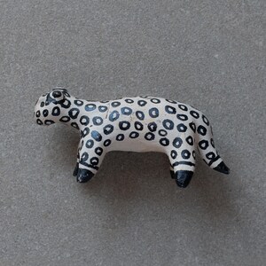 May include: A white ceramic animal figurine with black spots, resembling a leopard, standing on a gray surface.