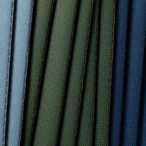 May include: Close-up of fabric swatches in shades of blue and green. The fabric has a textured, woven appearance.