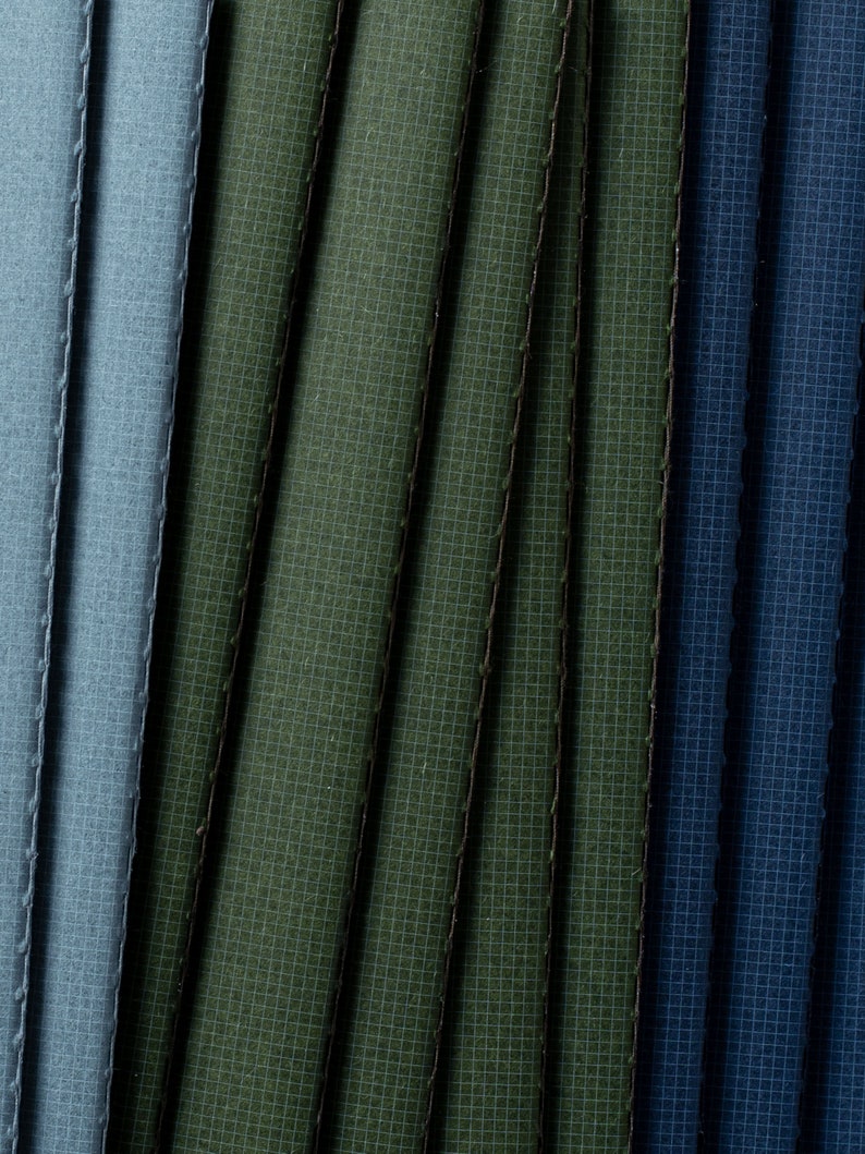 May include: Close-up of fabric swatches in shades of blue and green. The fabric has a textured, woven appearance.