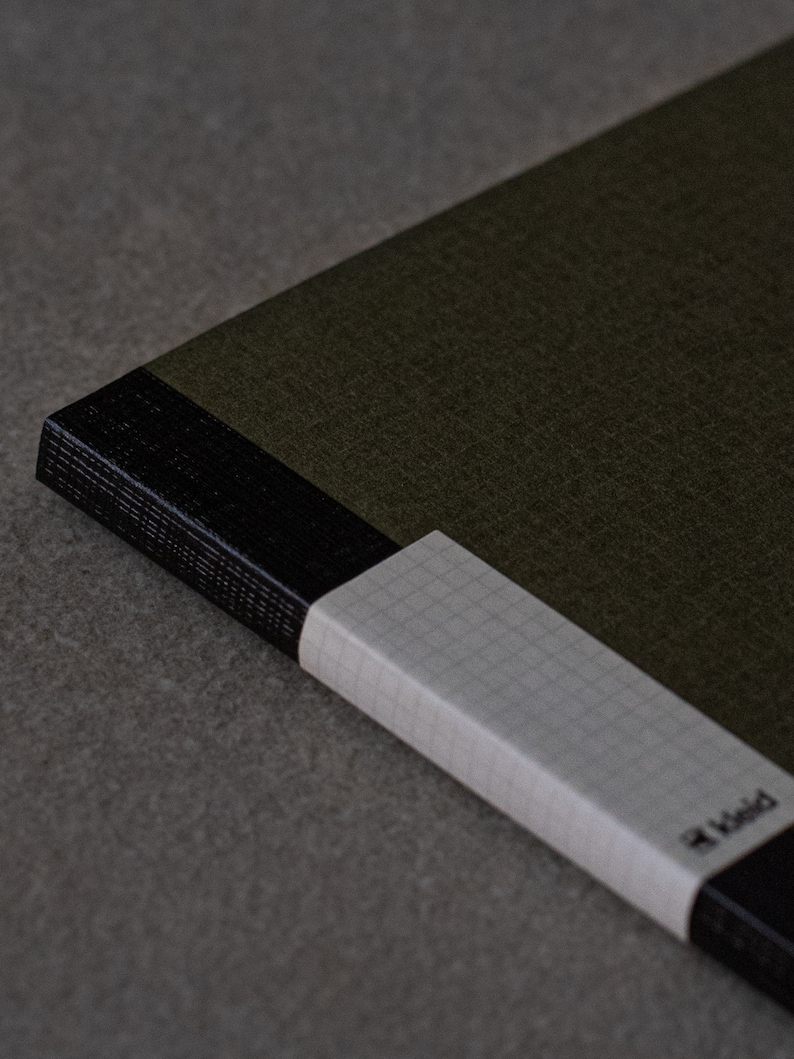 May include: A green notebook with a black spine and a white gridded page edge. The notebook has the word "Field" printed on the edge.