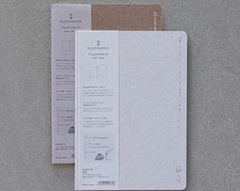 May include: Two notebooks with the brand name "KLEID NOTES" printed on the cover. The notebook on the left is brown and the notebook on the right is gray. Both notebooks have a tiny grid pattern and the text "Tiny grid notes B" printed on the cover.