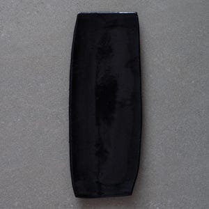 May include: A glossy black rectangular serving tray with rounded edges. The tray has a smooth, reflective surface and is set against a gray background. The tray's shape is elongated, suitable for serving appetizers or displaying small items.