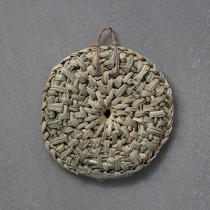 May include: A round, woven, straw coaster with a hole in the center and a brown string loop for hanging.