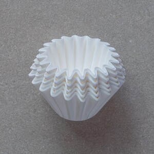 May include: A stack of white paper coffee filters, folded into a cone shape.