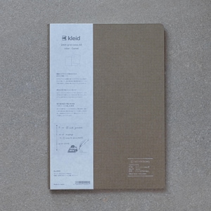 May include: A brown A5 notebook with a 2mm grid. The cover has a subtle texture and the text "kleid 2mm grid notes A5 color: Camel" is printed on the front. The back of the notebook has Japanese text and a small illustration of a quill pen and inkwell.