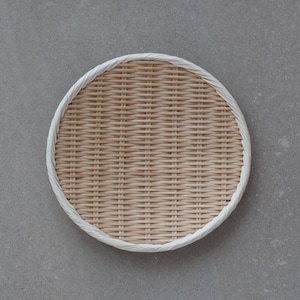 May include: A round, woven bamboo tray with a white rim. The tray is made of natural materials and has a rustic, handcrafted look.