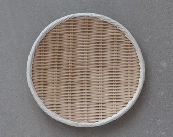 May include: A round, woven bamboo tray with a white rim. The tray is made of natural materials and has a rustic, handcrafted look.
