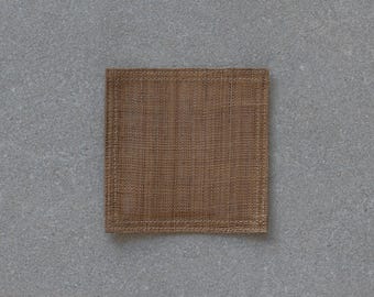 May include: A square, woven brown coaster. The coaster has a textured surface and a stitched border. The coaster is made of a natural fibre material and is designed to protect surfaces from drink rings.