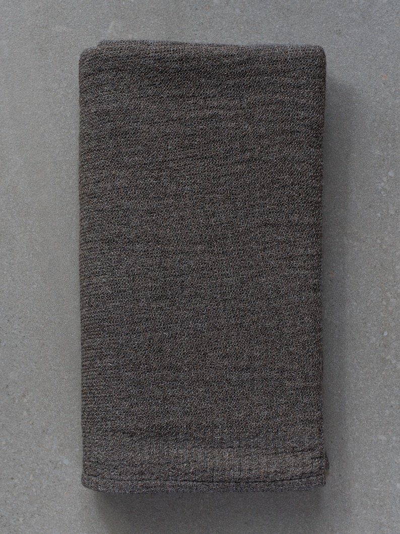 May include: A dark gray woven fabric napkin, folded in half, with a textured surface.