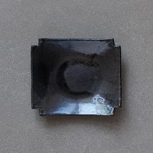 May include: A black square ceramic dish with a slightly raised rim and a glossy finish.