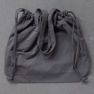 May include: A gray drawstring bag with two long straps. The bag is made of a soft, textured fabric.