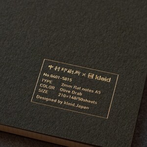 May include: A black notebook with gold lettering that reads "中村印刷所&times;kleid No.8401-5815 TYPE 2mm flat notes A5 COLOR Olive Drab SIZE 210x148/50sheets Designed by kleid. Japan"