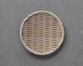 May include: A round, woven bamboo strainer with a natural brown color. The strainer is on a gray background.