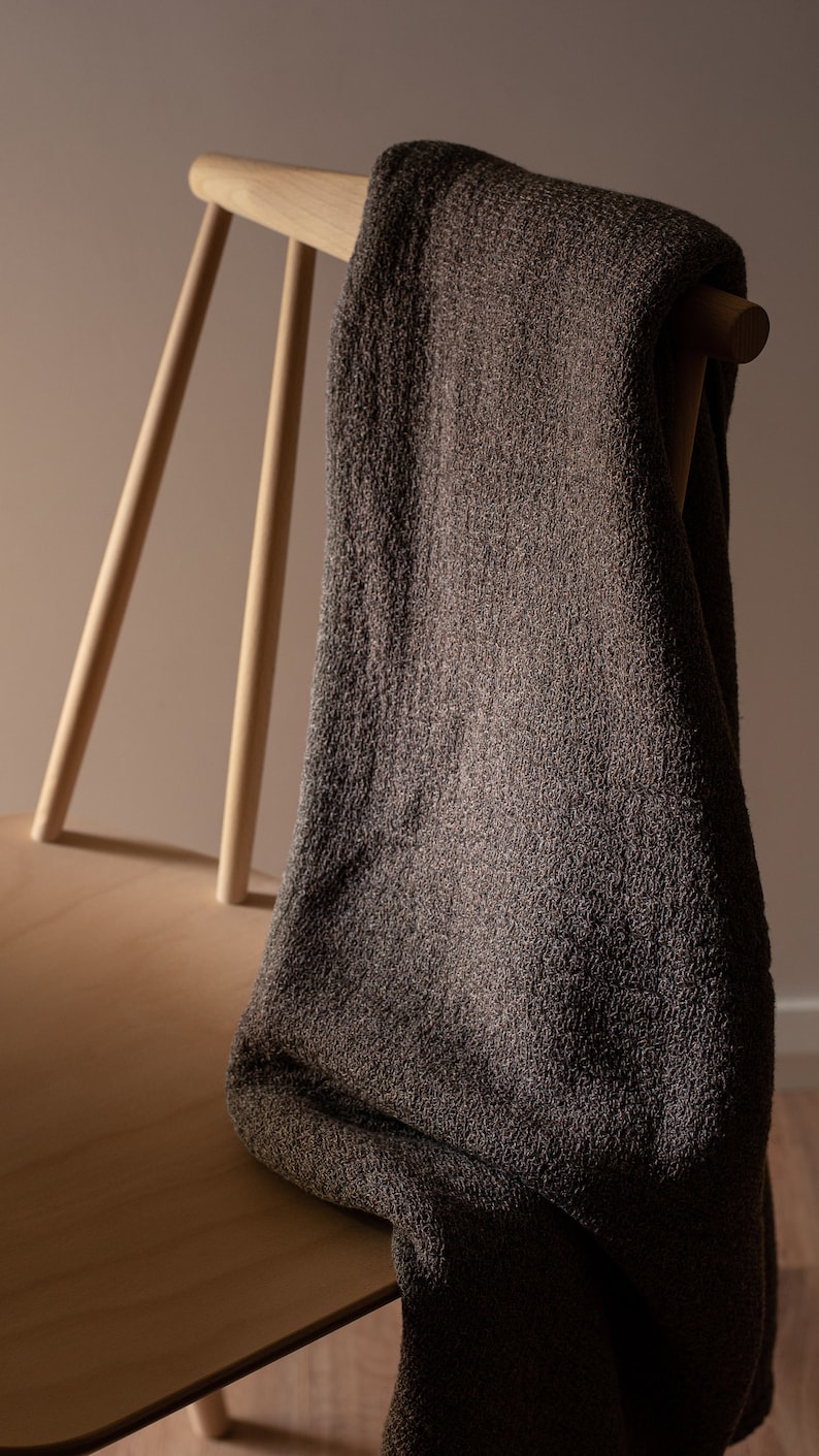 May include: A brown throw blanket draped over a wooden chair. The chair has a light wood finish and a simple design.