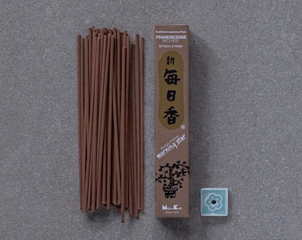 May include: A box of frankincense incense sticks with a brown and gold label that reads "New Daily Fragrance" in Japanese characters. The box is next to a small blue ceramic incense holder with a flower design.