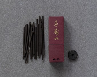 Può includere: Vista dall'alto di bastoncini di incenso marrone scuro, una scatola bordeaux con lettere dorate e un porta incenso nero su una superficie grigia. La scatola presenta testo giapponese. I bastoncini di incenso sono disposti in modo sparso.