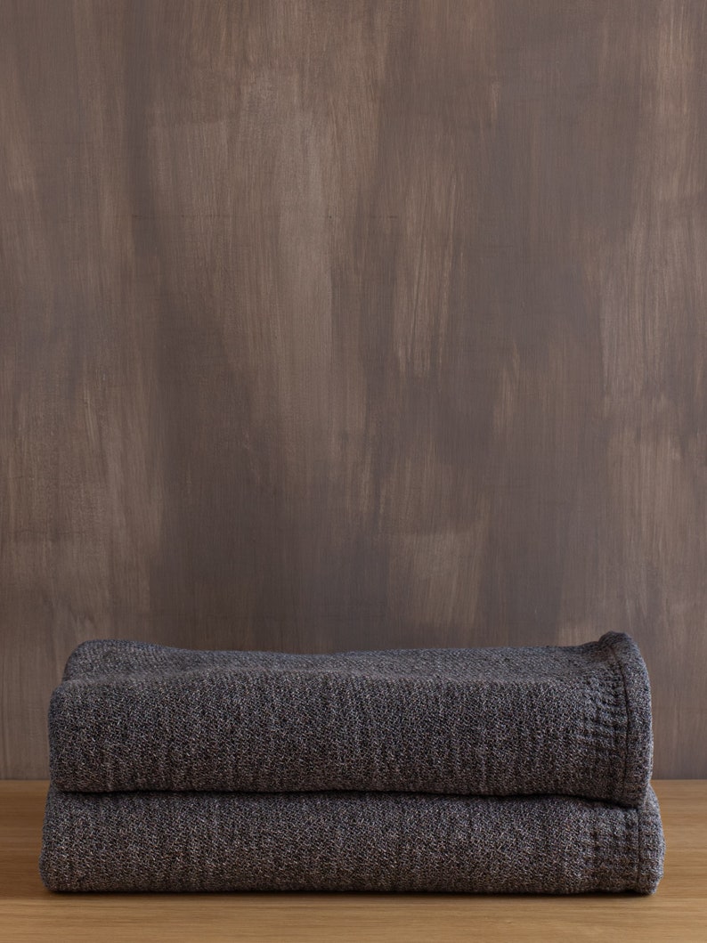 May include: Two folded gray knitted blankets stacked on top of each other on a wooden surface.